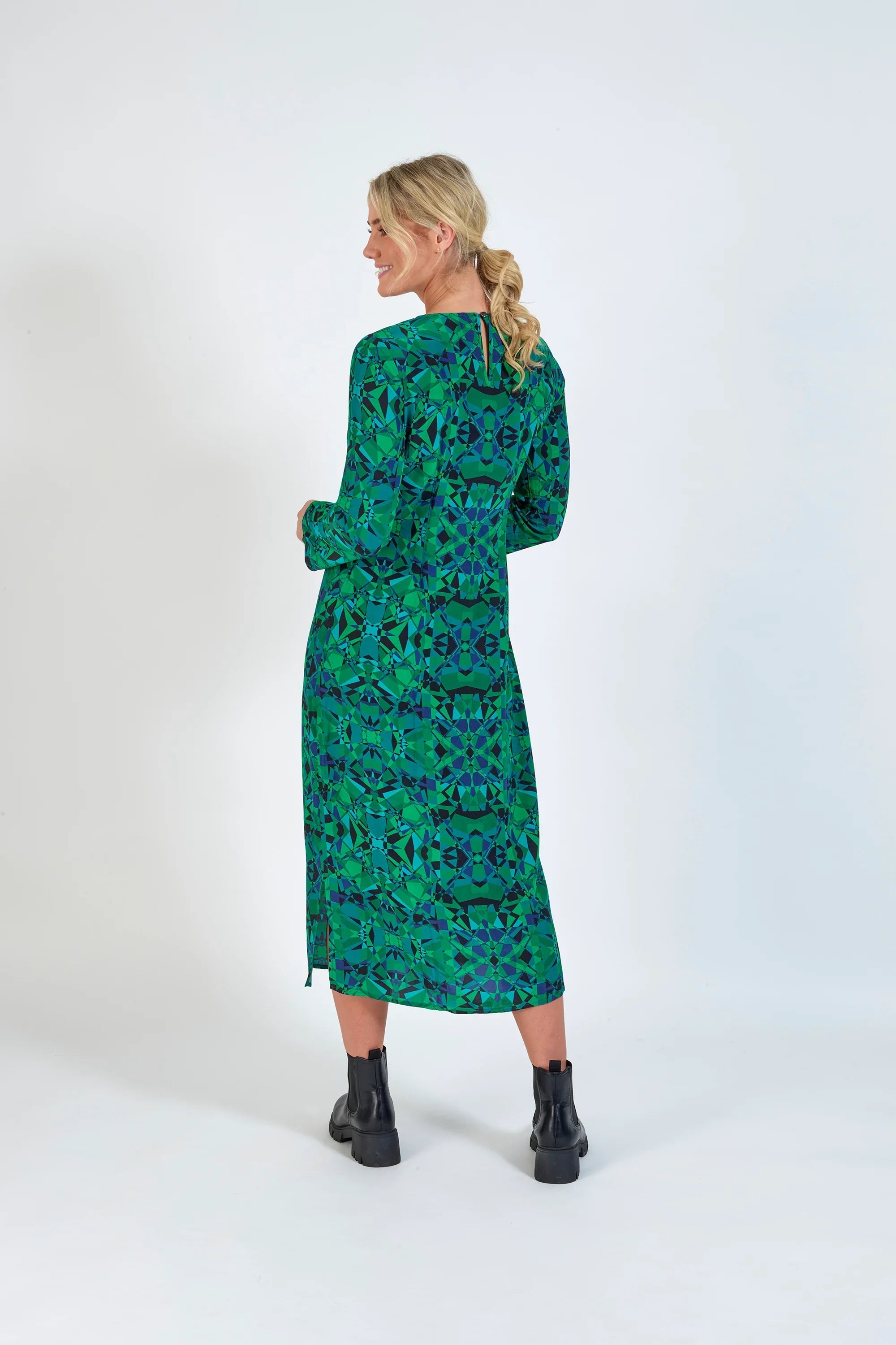 Woman in green geometric long-sleeve midi dress, side view, with black ankle boots