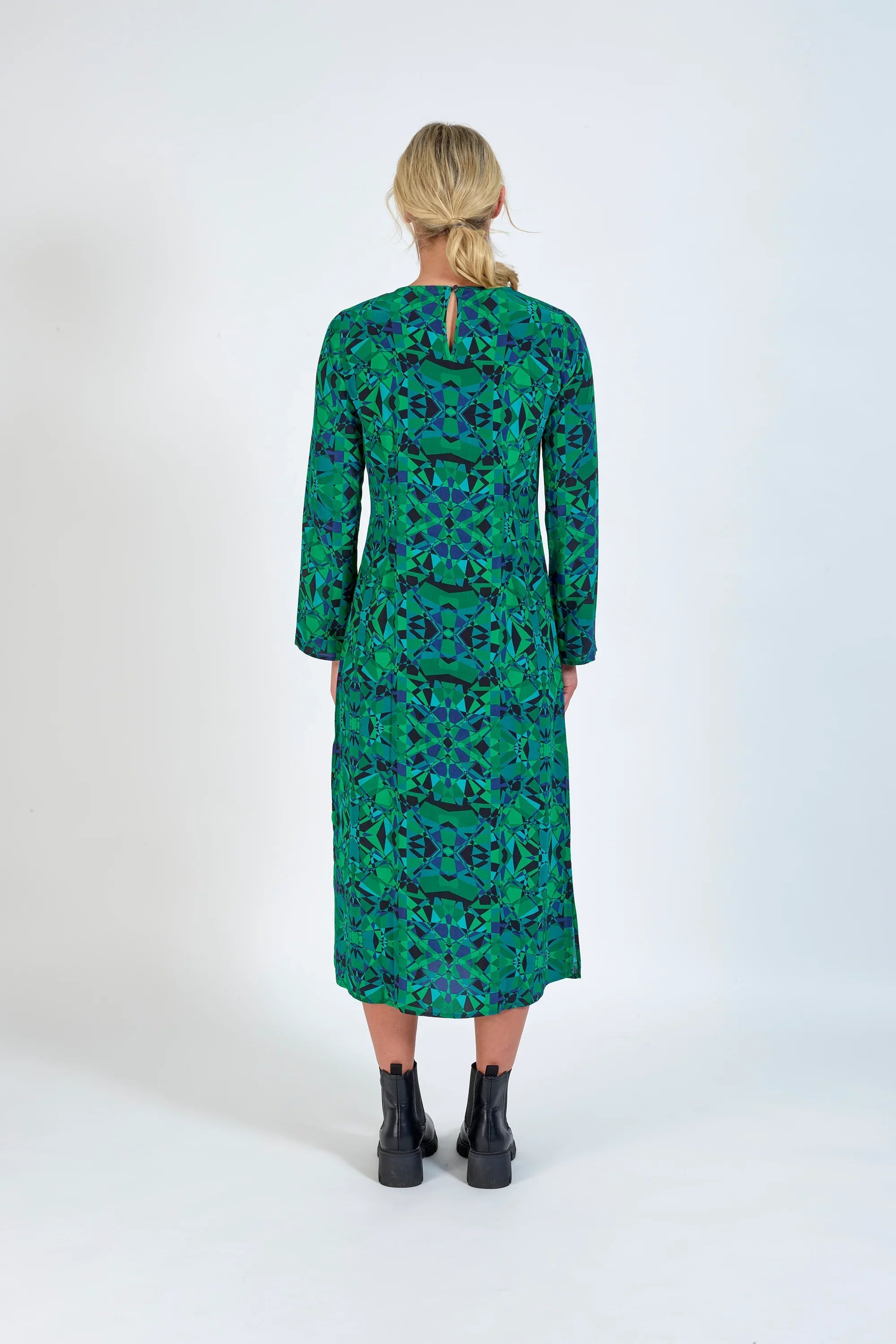 Woman in green geometric long sleeve midi dress and black boots, back view