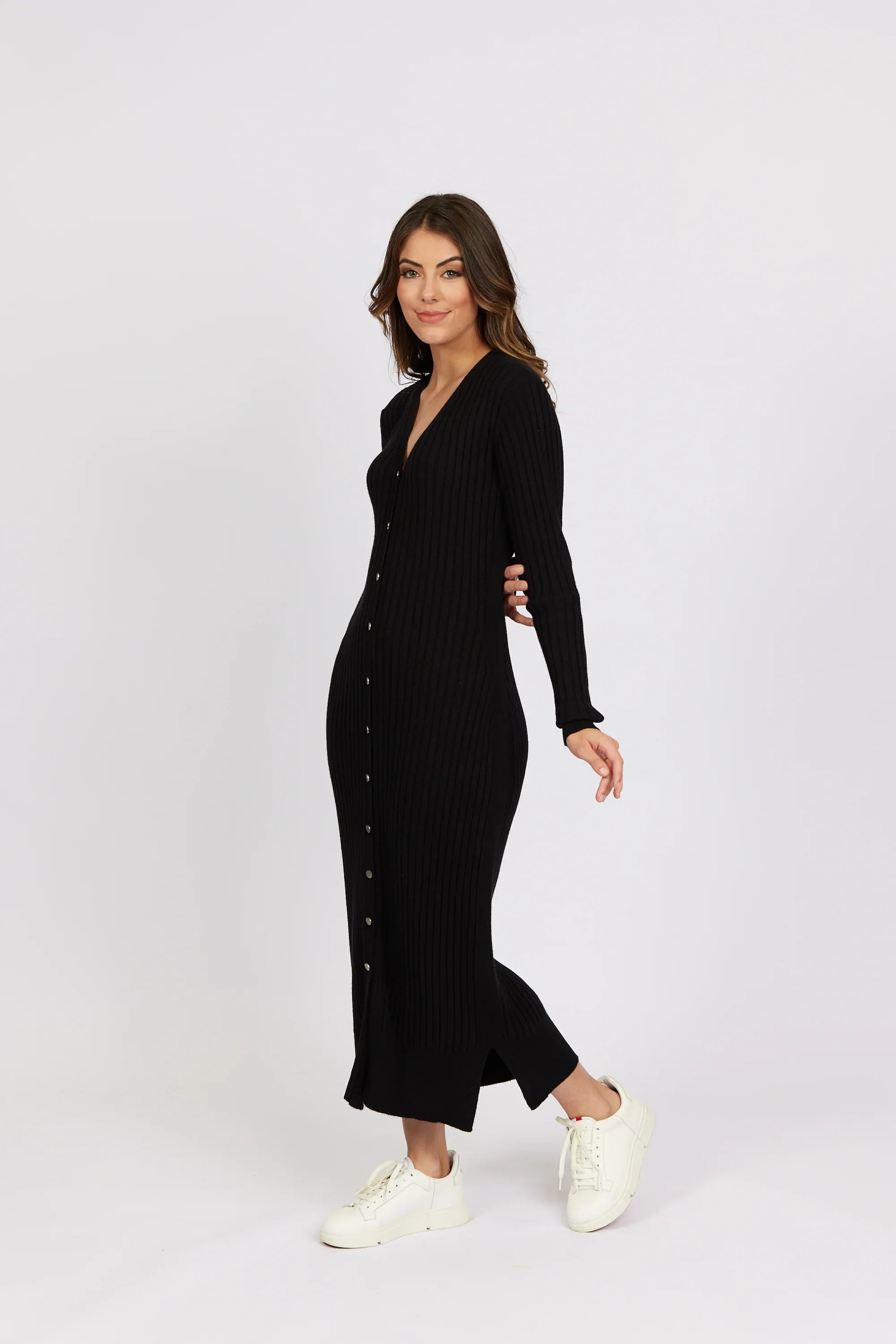 Woman wearing a black ribbed button-front knit dress with long sleeves and white sneakers