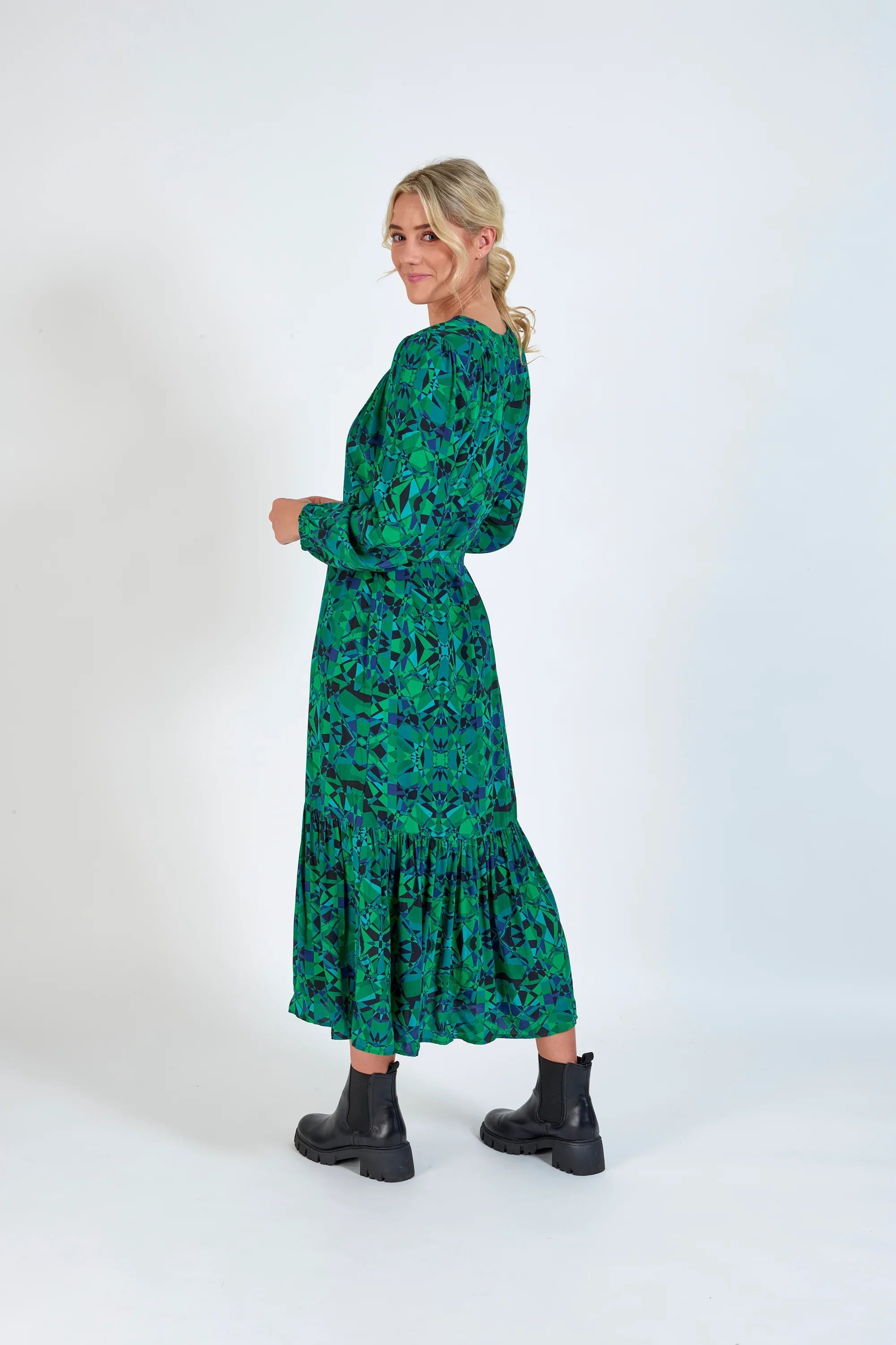 Woman in a green patterned long-sleeve midi dress with ruffle hem, styled with black boots