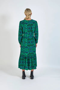 Woman in green geometric print midi dress with long sleeves and black ankle boots, back view