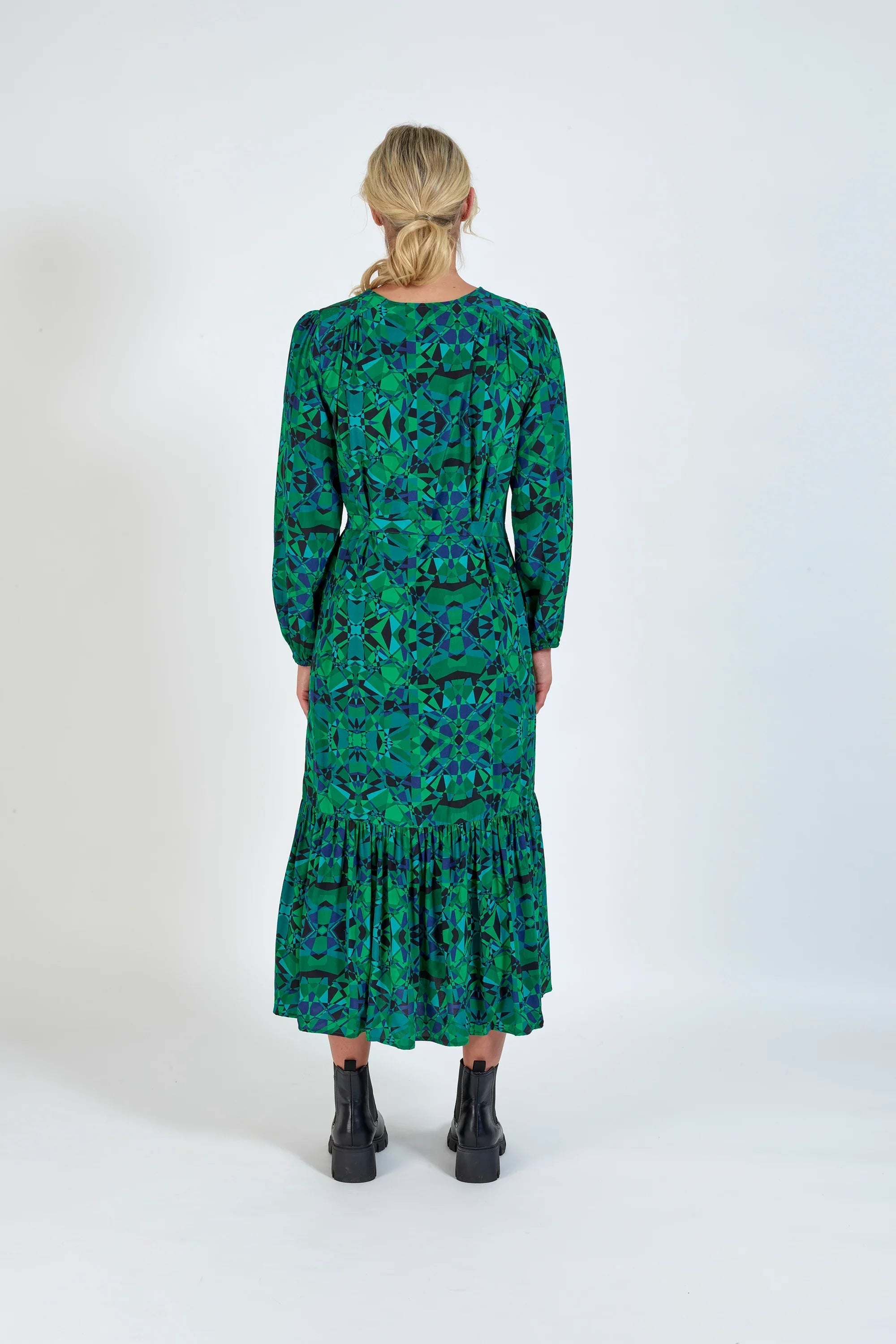 Woman in green geometric print midi dress with long sleeves and black ankle boots, back view