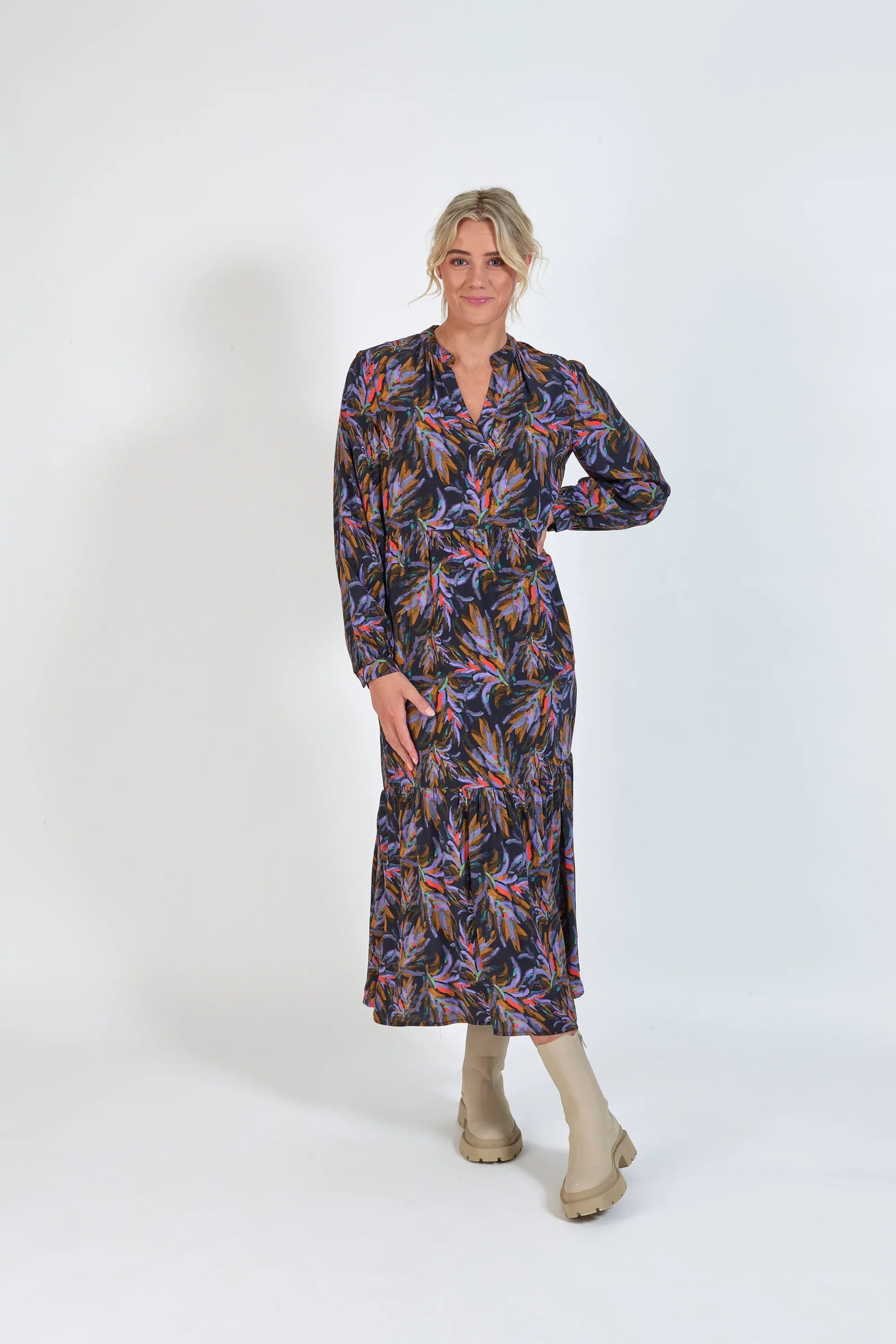 Woman in long-sleeve floral print midi dress with neutral boots, standing against white background
