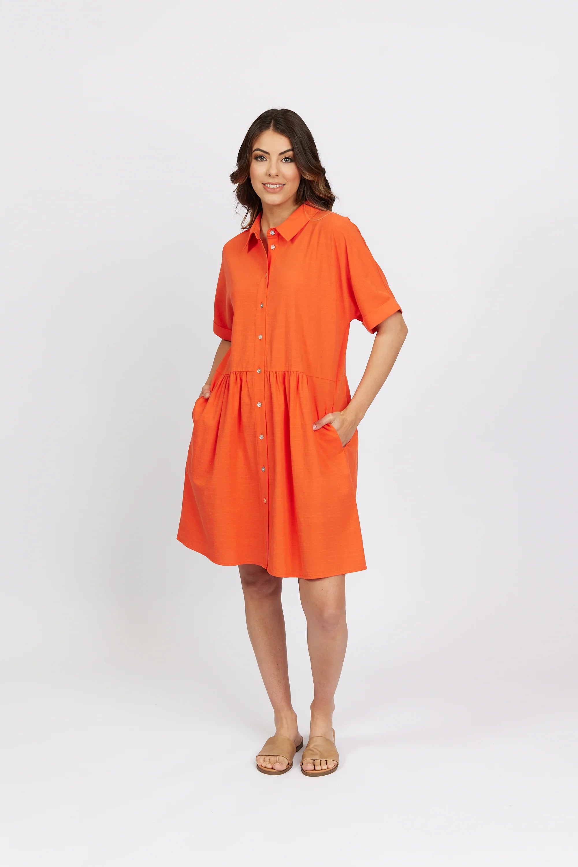 Woman wearing a bright orange short sleeve cocoon dress with buttons and side pockets