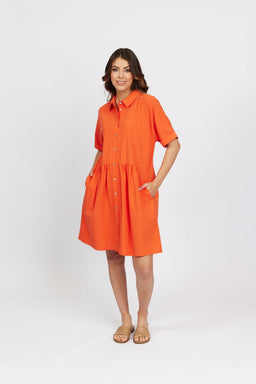 Woman wearing a bright orange short sleeve cocoon dress with buttons and side pockets