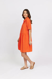 Woman in short-sleeve orange cocoon dress and tan sandals on white background