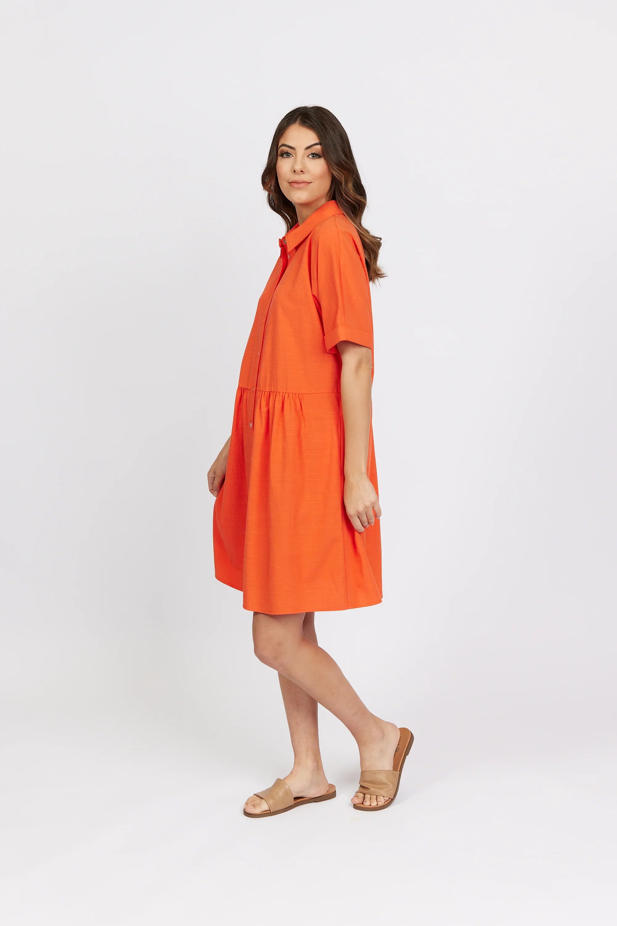 Woman in short-sleeve orange cocoon dress and tan sandals on white background