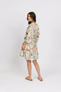 Woman wearing a short floral dress with kimono sleeves, standing in a studio setting
