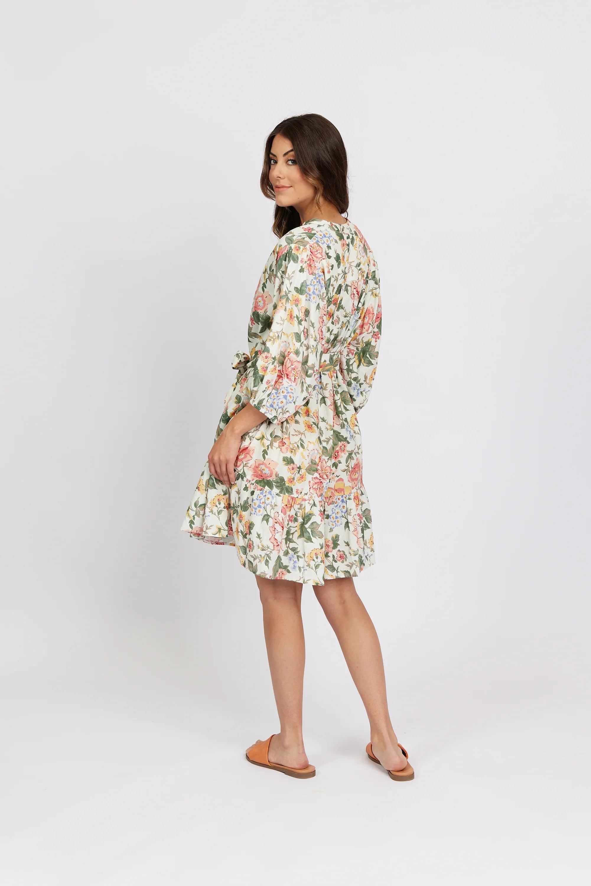 Woman wearing a short floral dress with kimono sleeves, standing in a studio setting