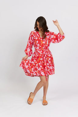 Woman wearing a vibrant floral print knee-length dress with long sleeves and tie waist