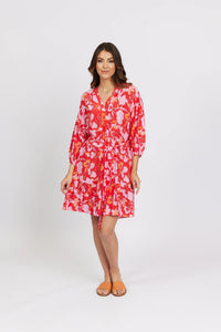 Woman wearing a pink and red floral print dress with tie waist and ruffle hem, studio background