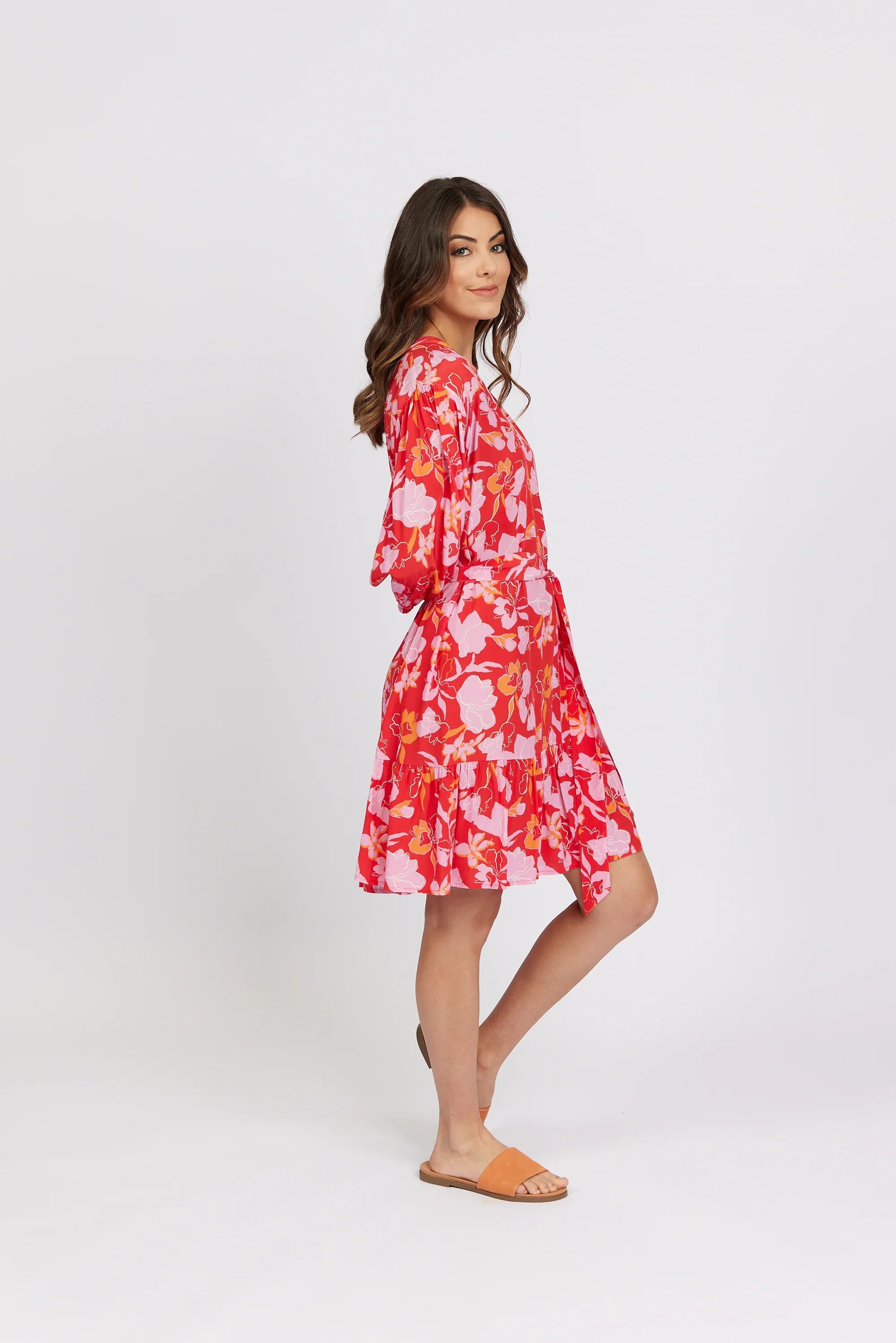Woman wearing a vibrant floral knee-length dress with pink and orange patterns, side view