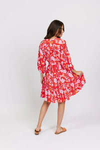 Woman in a red floral dress with long sleeves and ruffled skirt, posing against a white background