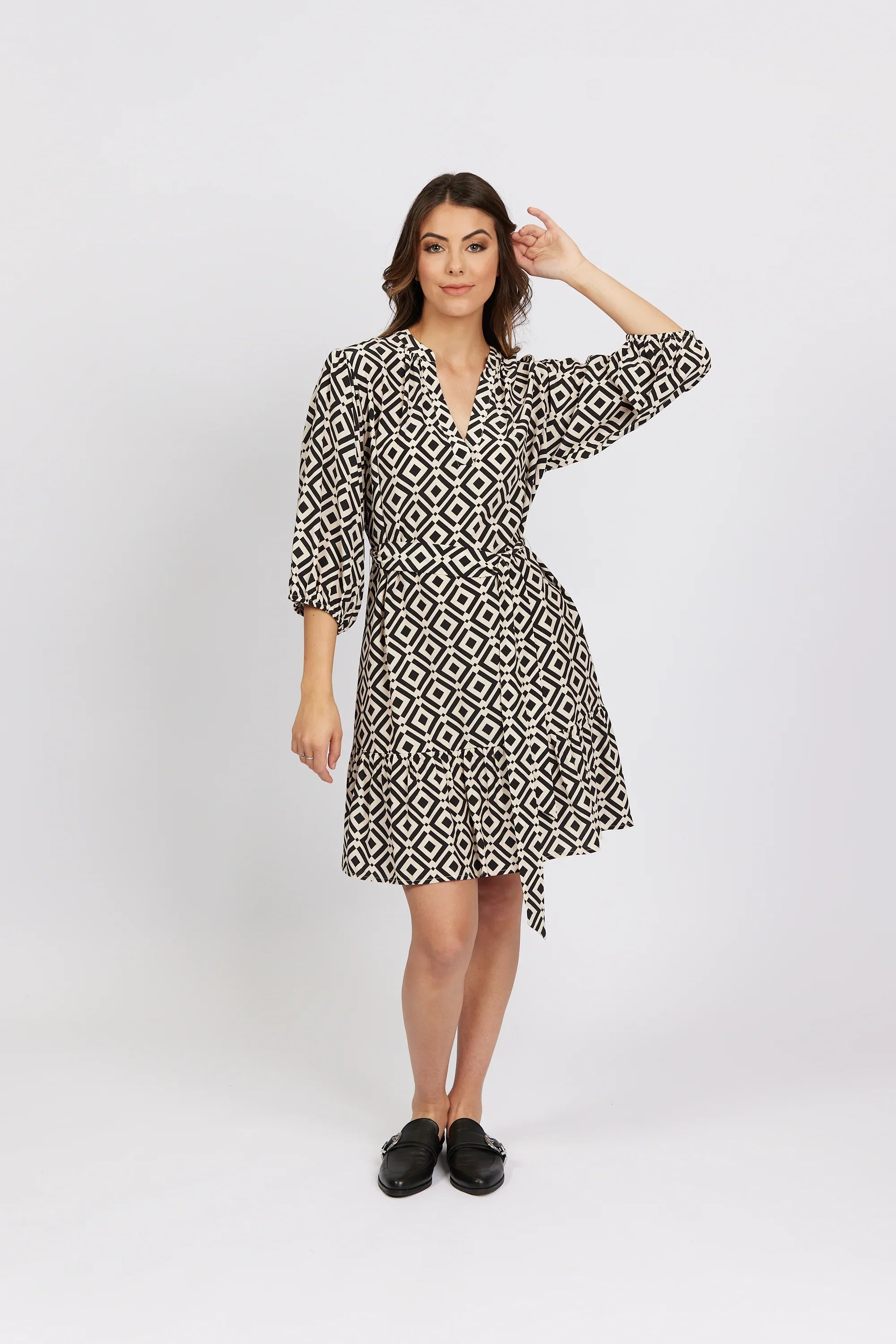 Woman wearing a geometric print wrap dress with three-quarter sleeves in a studio setting.