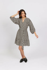 Woman in geometric print wrap dress with long sleeves and black loafers, studio background