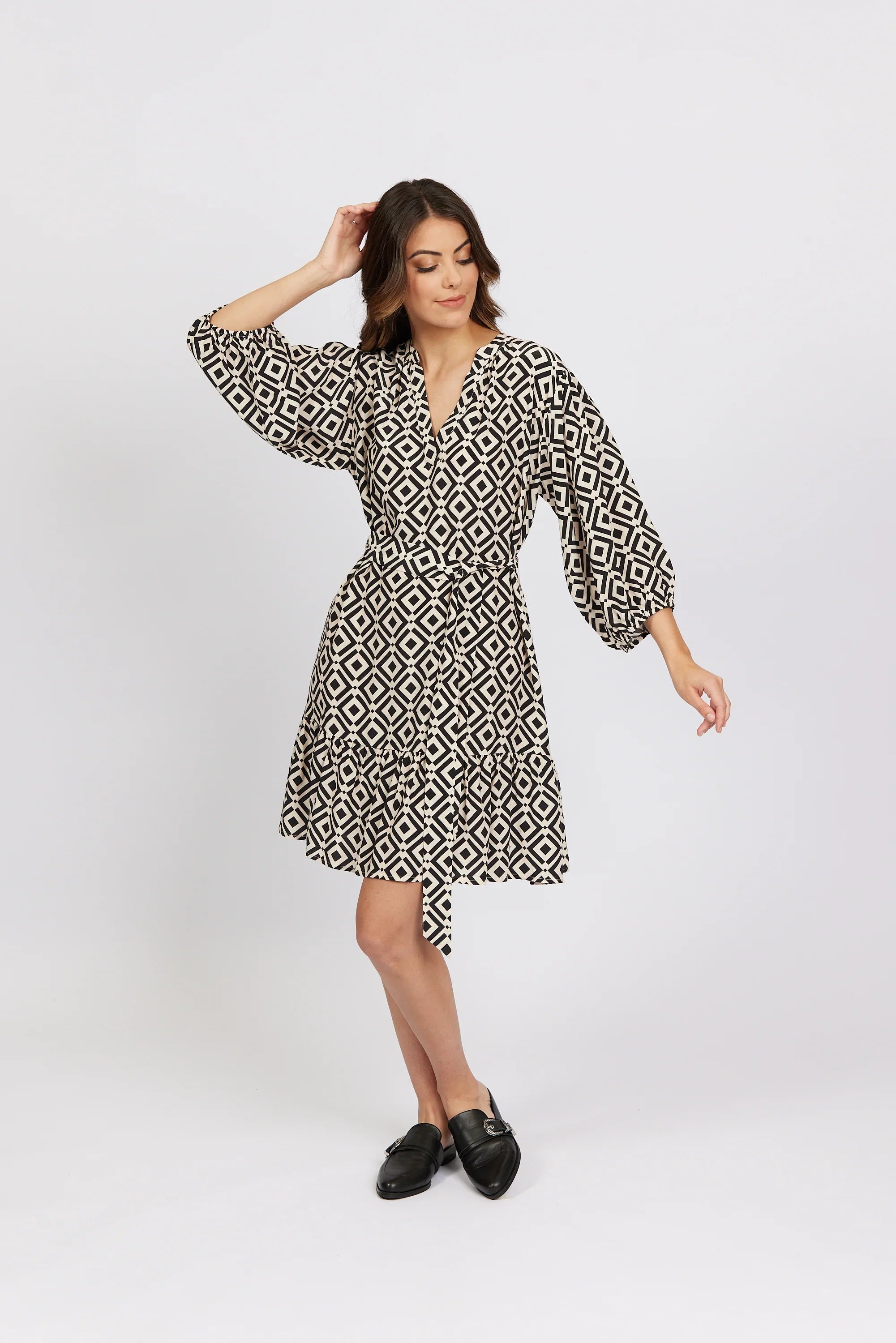 Woman in geometric print wrap dress with long sleeves and black loafers, studio background