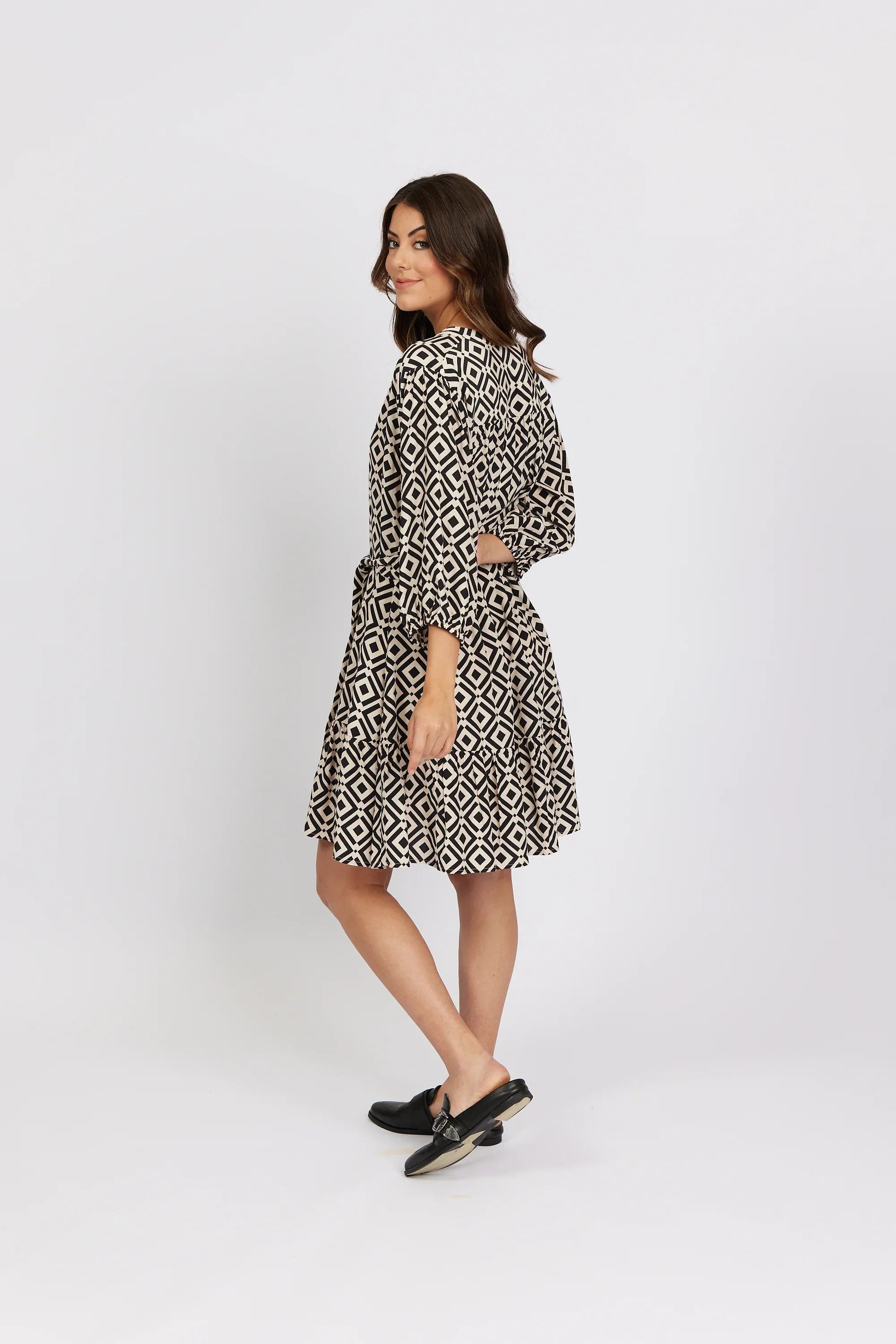 Woman in black and white geometric print dress with long sleeves, posing sideways.