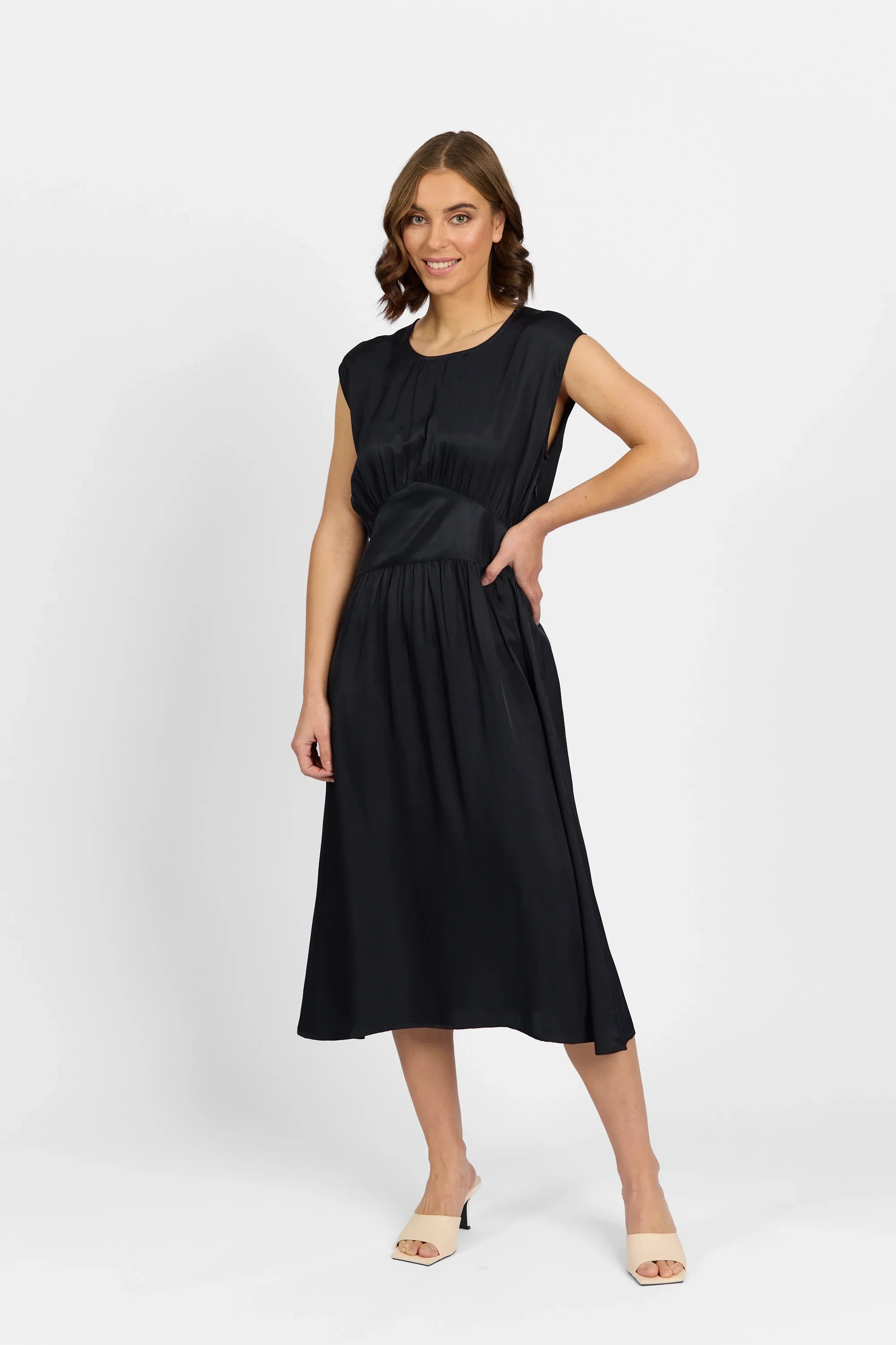 Woman wearing black midi sleeveless dress with gathered waist, posing in studio