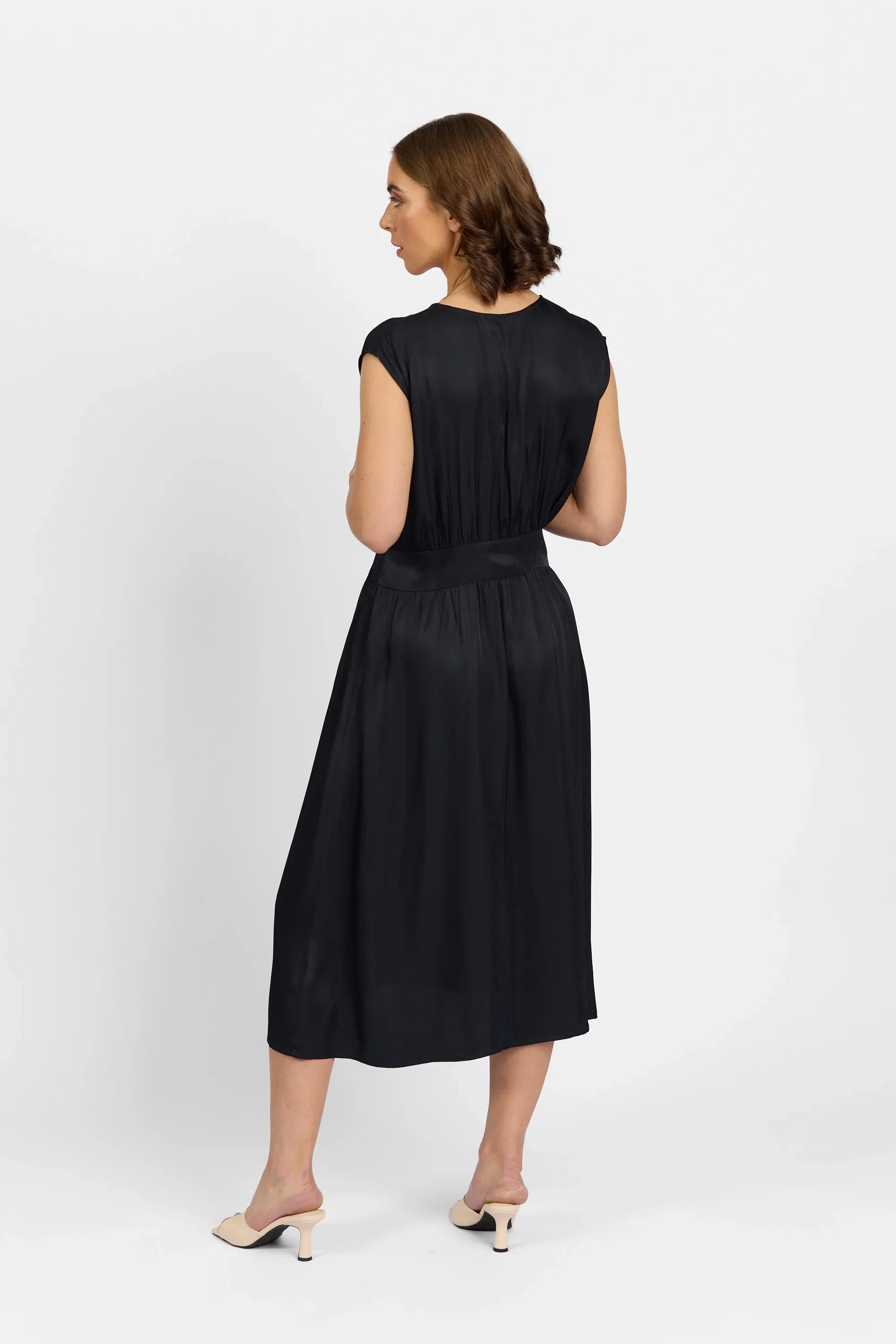 Woman modeling sleeveless black midi dress with gathered waist, photographed from the back