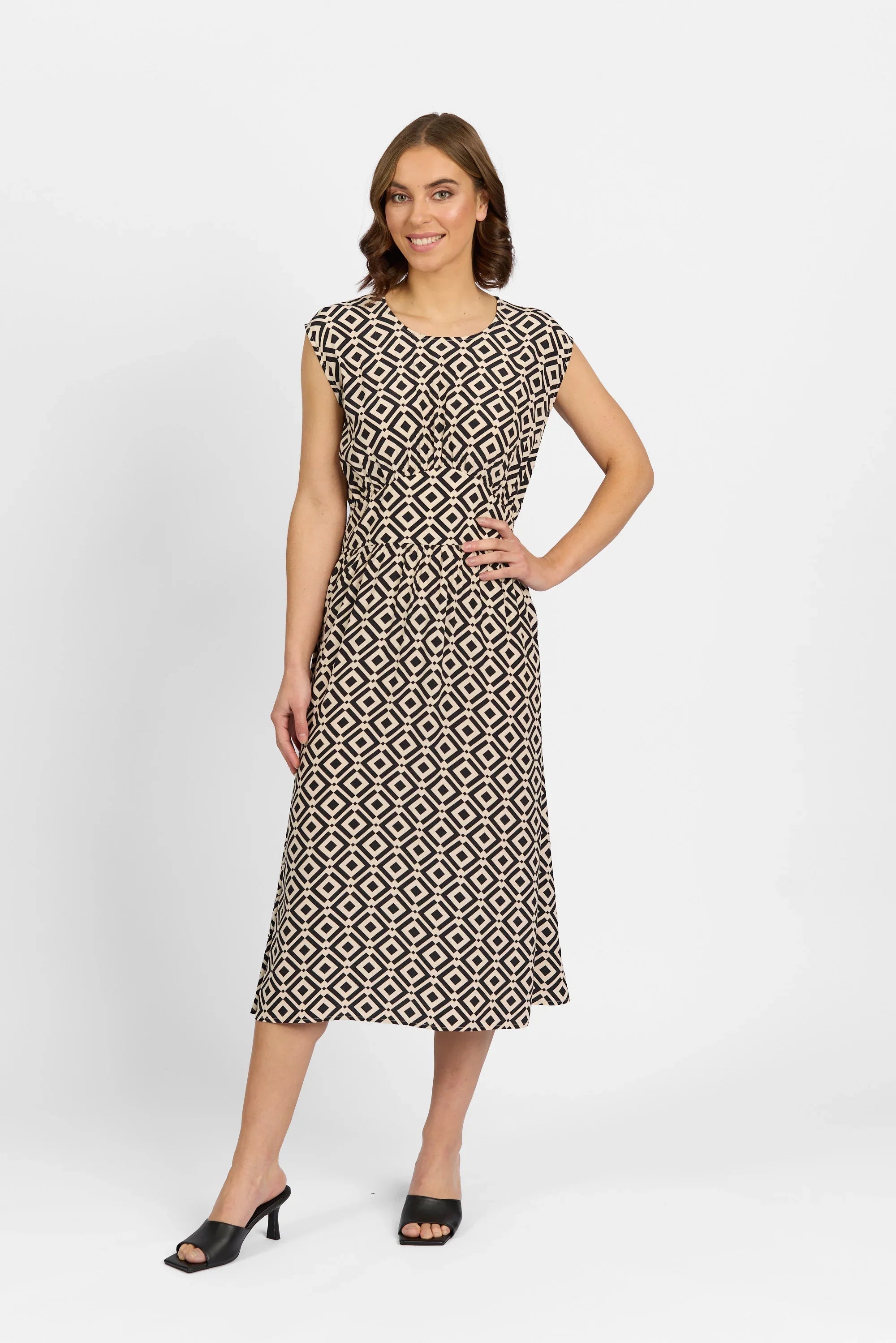 Woman wearing a sleeveless geometric print midi dress with black heeled sandals