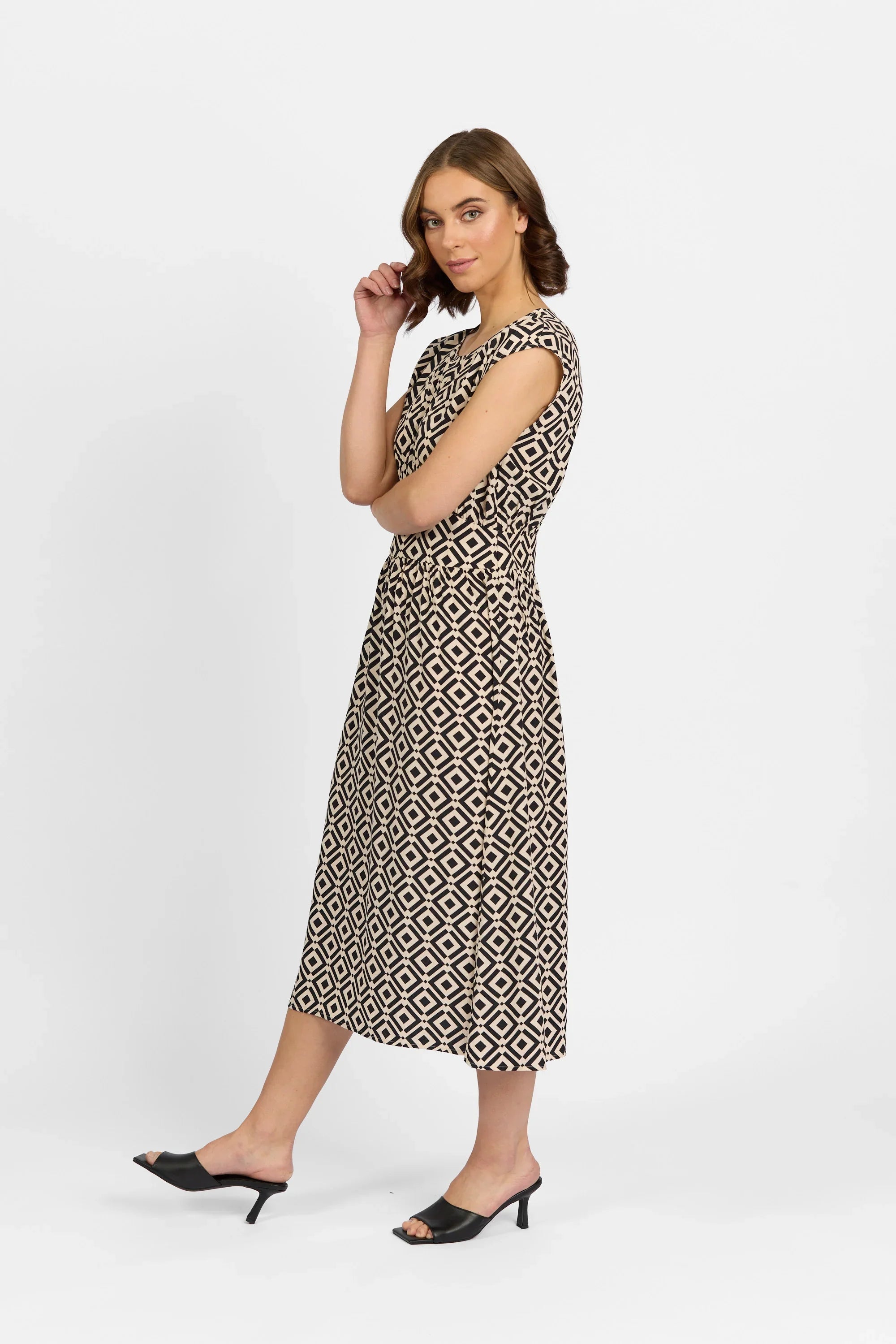 Woman in geometric print midi dress with cap sleeves and black heeled sandals, white background