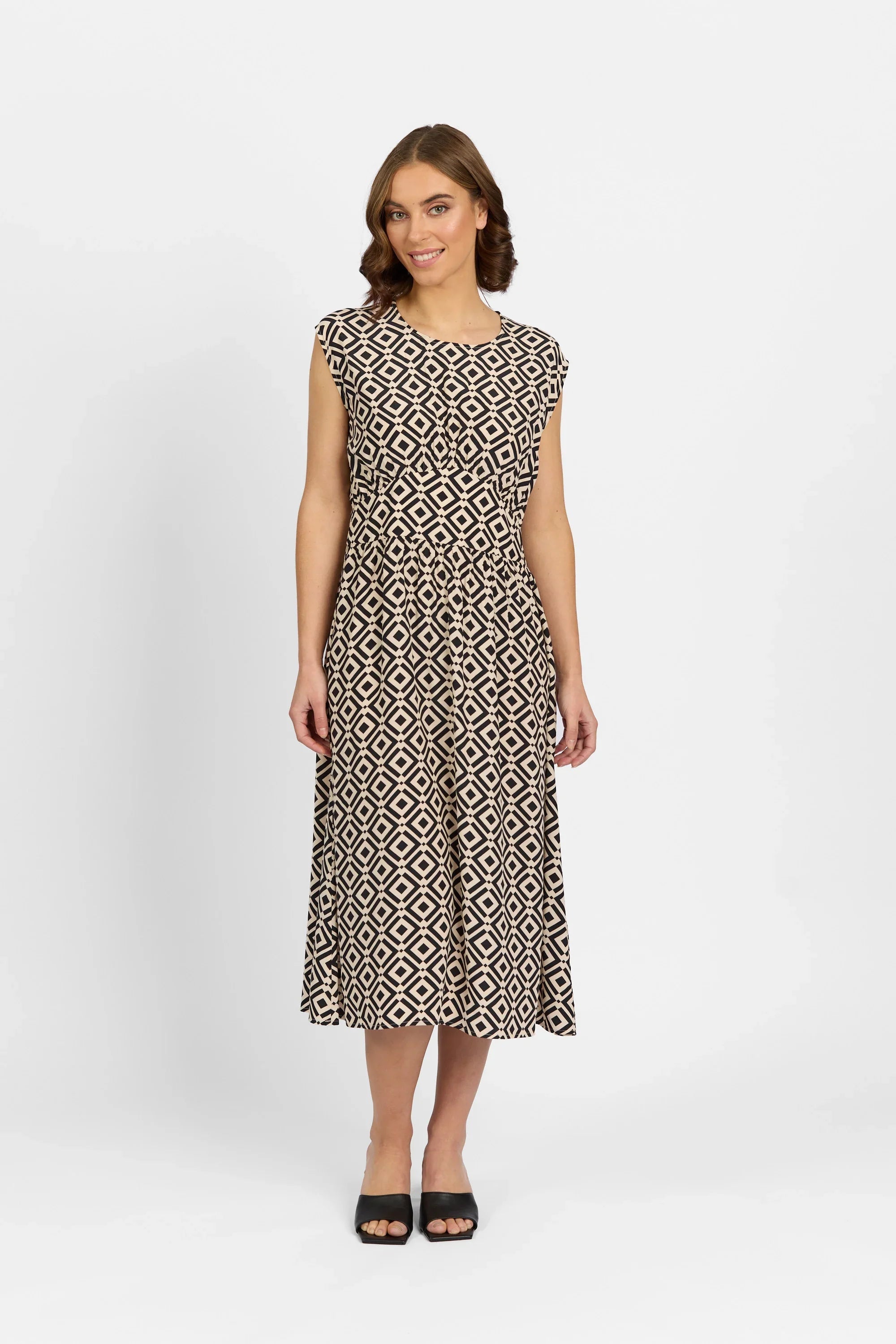 Woman wearing a black and beige geometric print midi dress, cap sleeves, black sandals