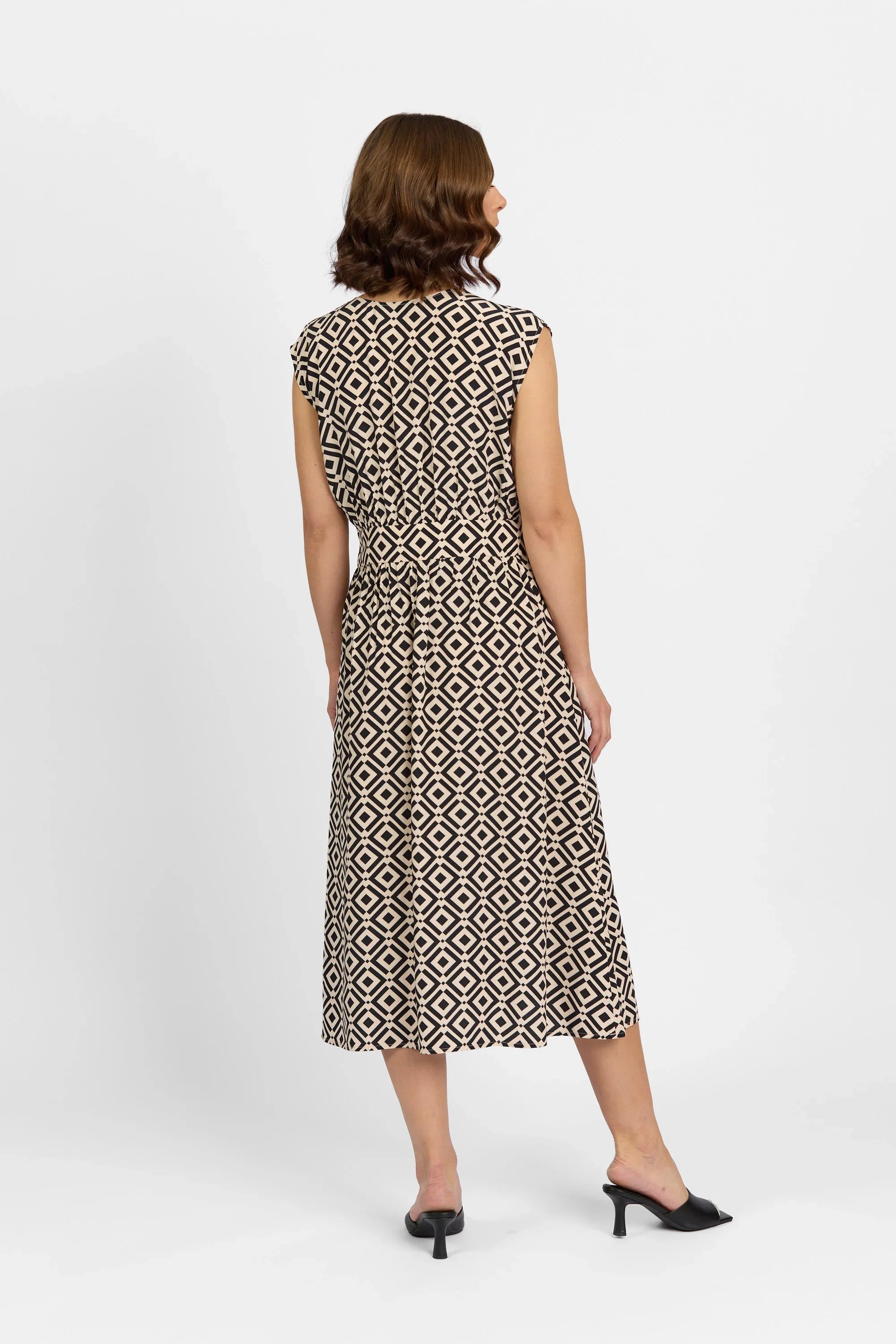 Woman wearing sleeveless black and beige geometric print midi dress with tie waist, back view
