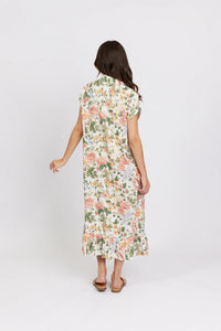 Woman wearing a long, floral print dress with ruffled hem, standing against white background.