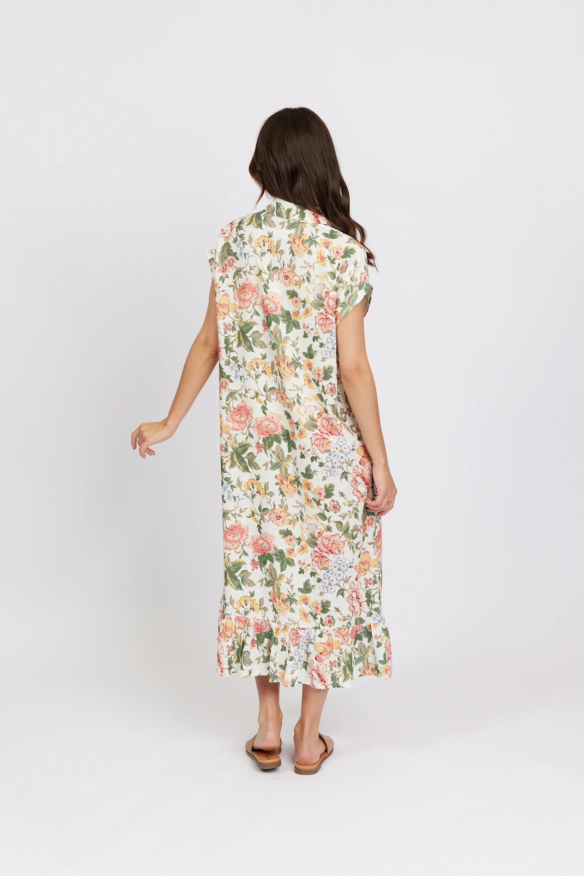 Woman wearing a long, floral print dress with ruffled hem, standing against white background.