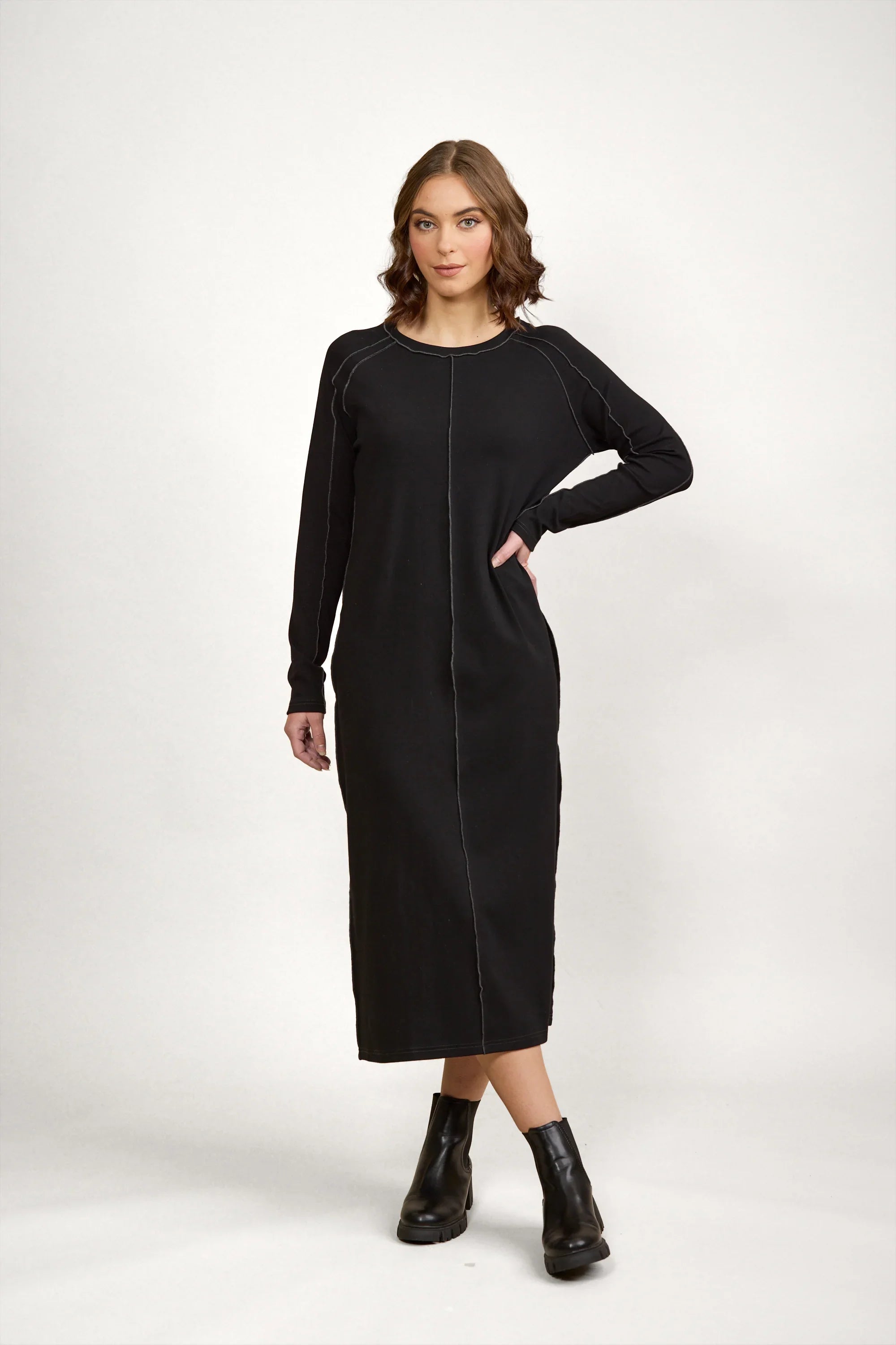 Woman wearing long sleeve black midi dress with contrast stitching and black ankle boots