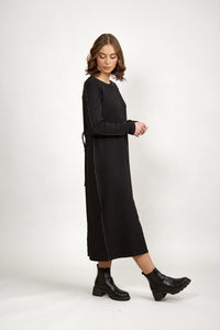 Woman wearing a long sleeve black midi dress with contrast stitching and ankle boots