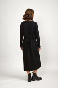 Woman in long sleeve black midi dress with visible seam details, back tie, and ankle boots