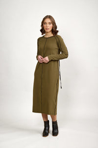 Woman in olive green long sleeve midi dress with black seam detail, standing indoors