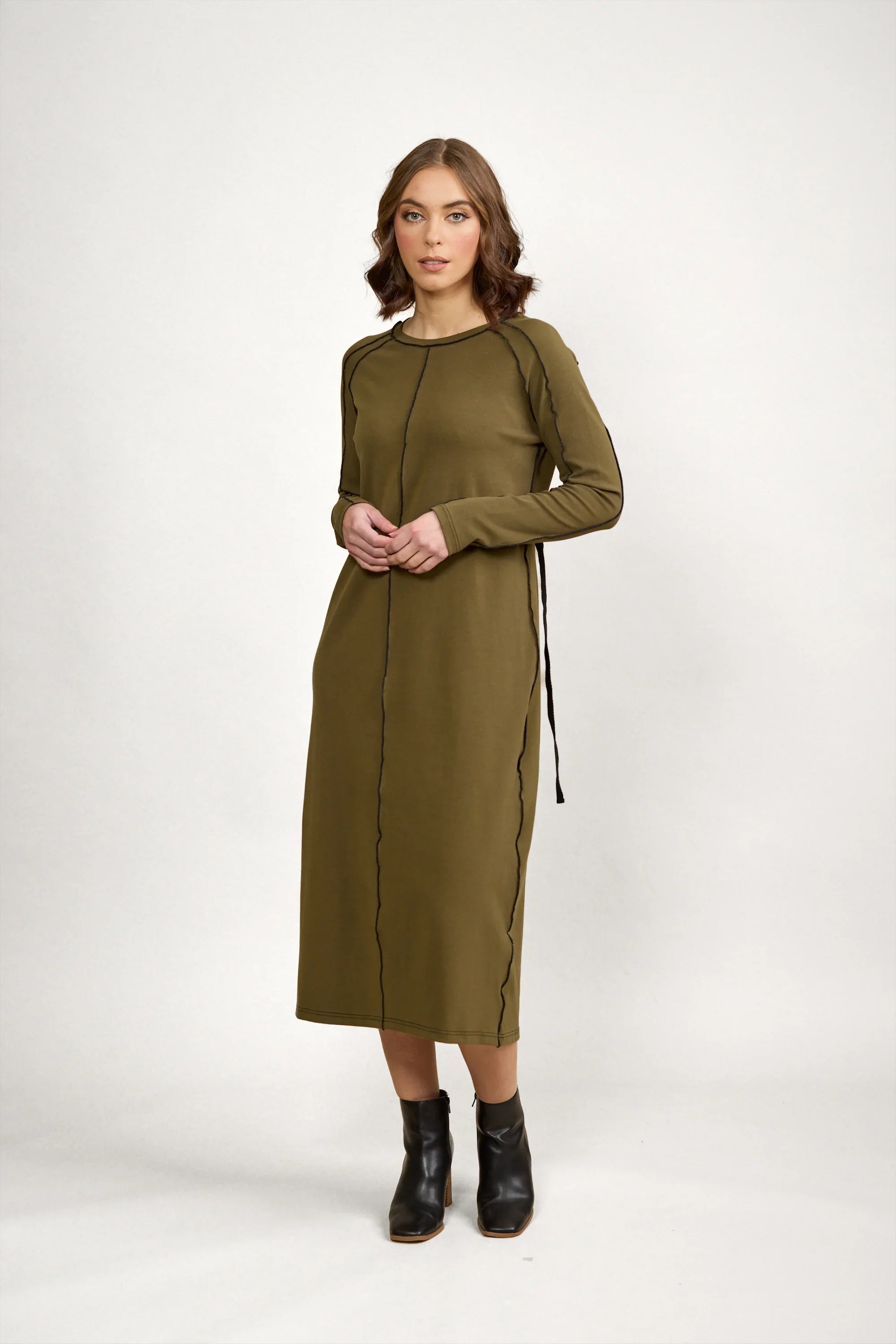 Woman in olive green long sleeve midi dress with black seam detail, standing indoors