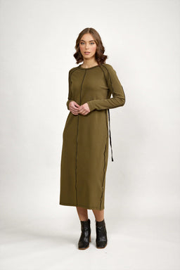 Woman in olive green long sleeve midi dress with black seam detail, standing indoors