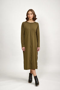 Woman wearing olive green long sleeve midi dress with black seam details and black ankle boots, standing against a plain white background.