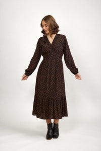 Woman wearing a mocha brown long sleeve midi dress with abstract print and black ankle boots