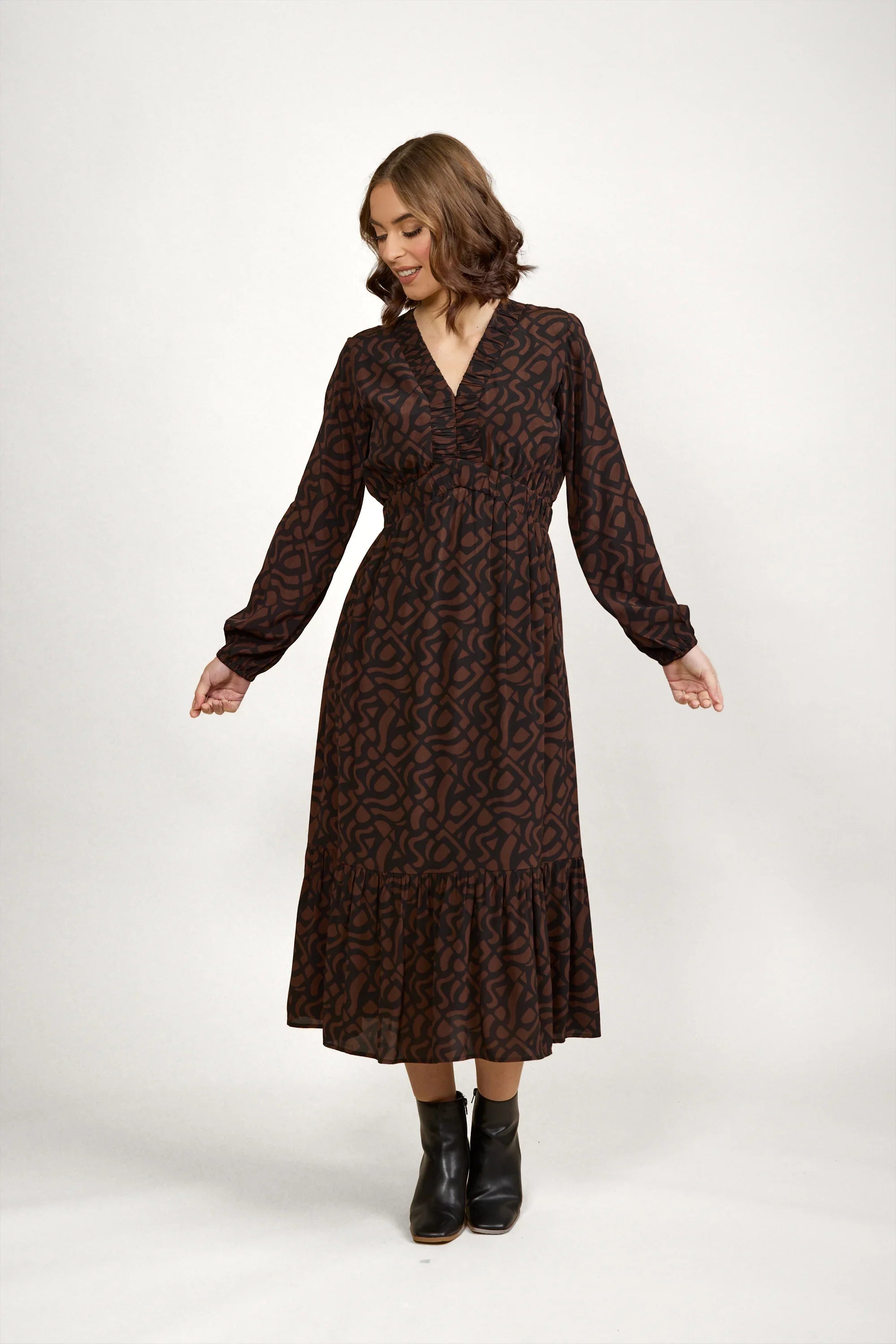 Woman wearing a mocha brown long sleeve midi dress with abstract print and black ankle boots