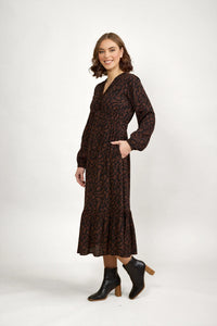 Woman wearing a mocha brown long sleeve midi dress with abstract print and ankle boots