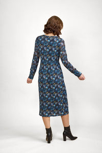 Woman wearing a long-sleeve blue floral midi dress and black ankle boots, back view