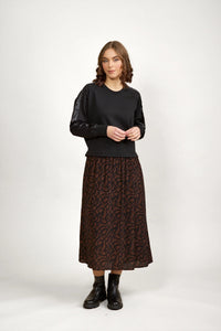 Woman wearing a black long-sleeve top and mocha brown patterned midi skirt with black boots