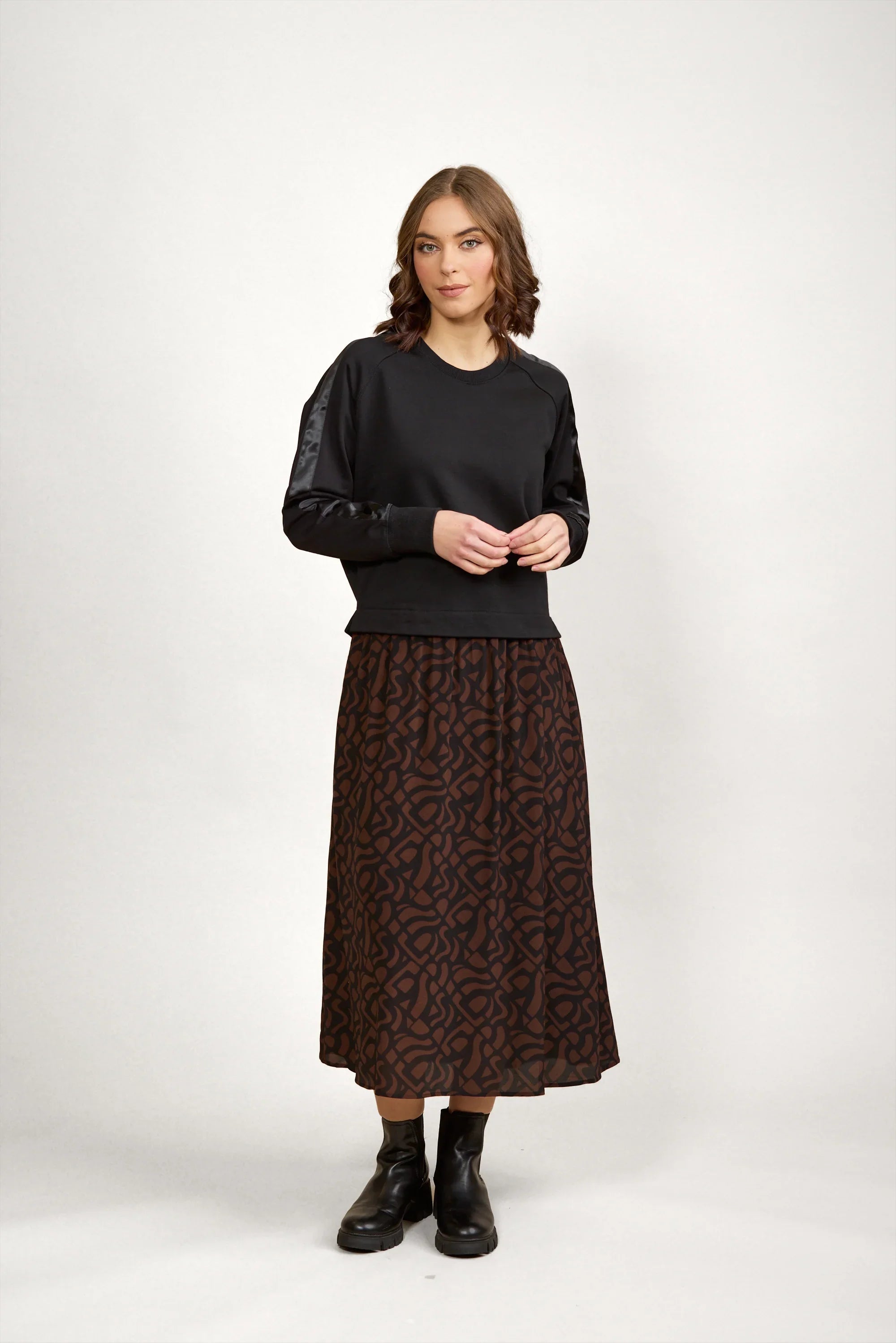 Woman wearing a black long-sleeve top and mocha brown patterned midi skirt with black boots