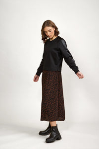 Woman wearing a black long-sleeve top and a brown patterned midi skirt with black boots
