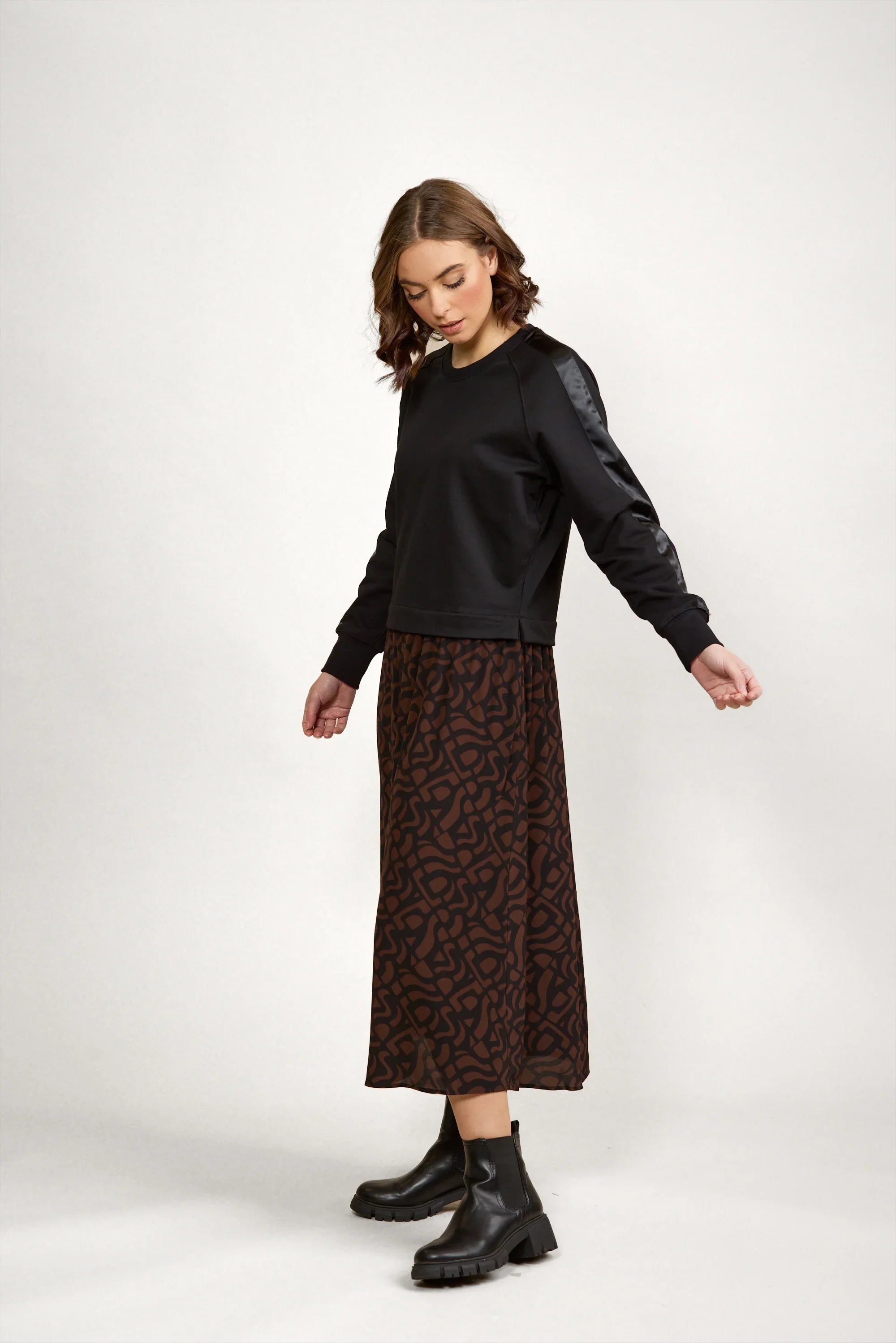 Woman wearing a black long-sleeve top and a brown patterned midi skirt with black boots