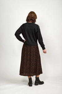Back view of woman wearing black long sleeve top, brown abstract print midi skirt, and black boots