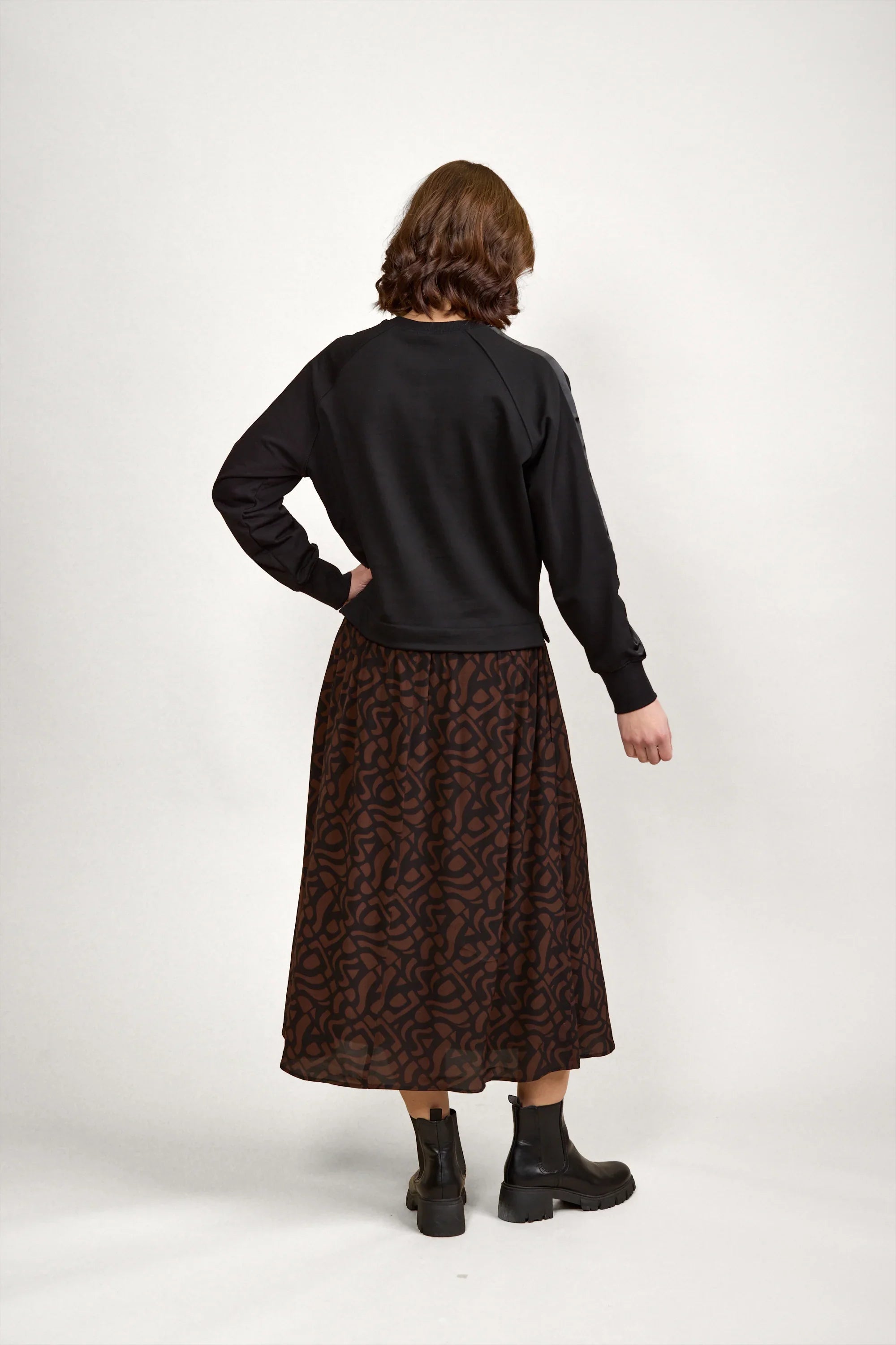 Back view of woman wearing black long sleeve top, brown abstract print midi skirt, and black boots