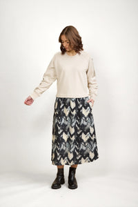 Woman wearing beige long sleeve top and black patterned midi skirt with black ankle boots
