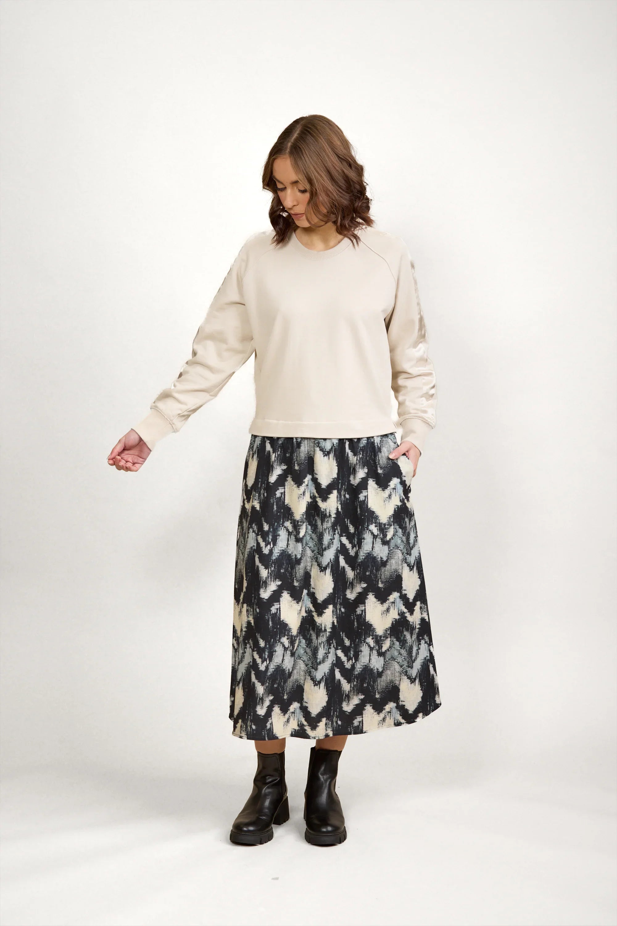 Woman wearing beige long sleeve top and black patterned midi skirt with black ankle boots