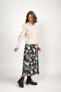 Woman in a beige long-sleeve top and abstract patterned midi skirt with black boots