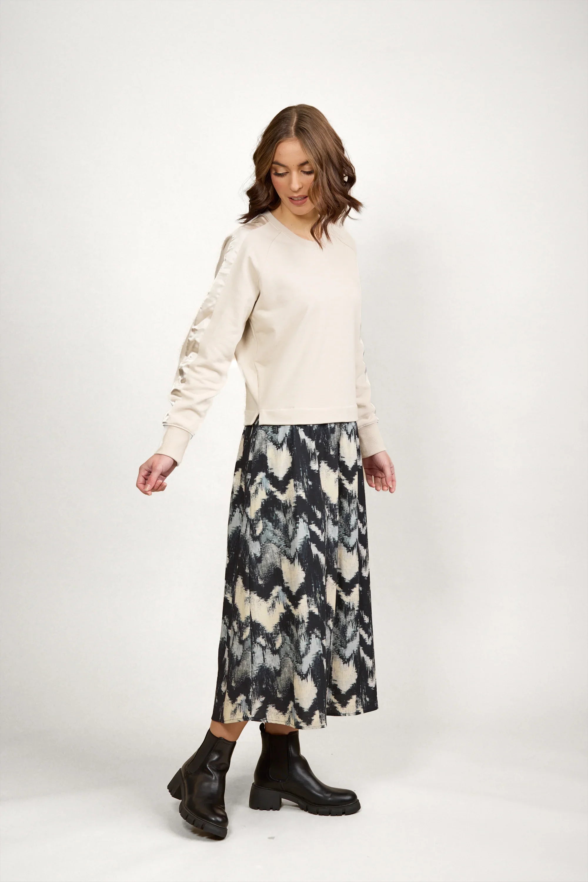 Woman in a beige long-sleeve top and abstract patterned midi skirt with black boots